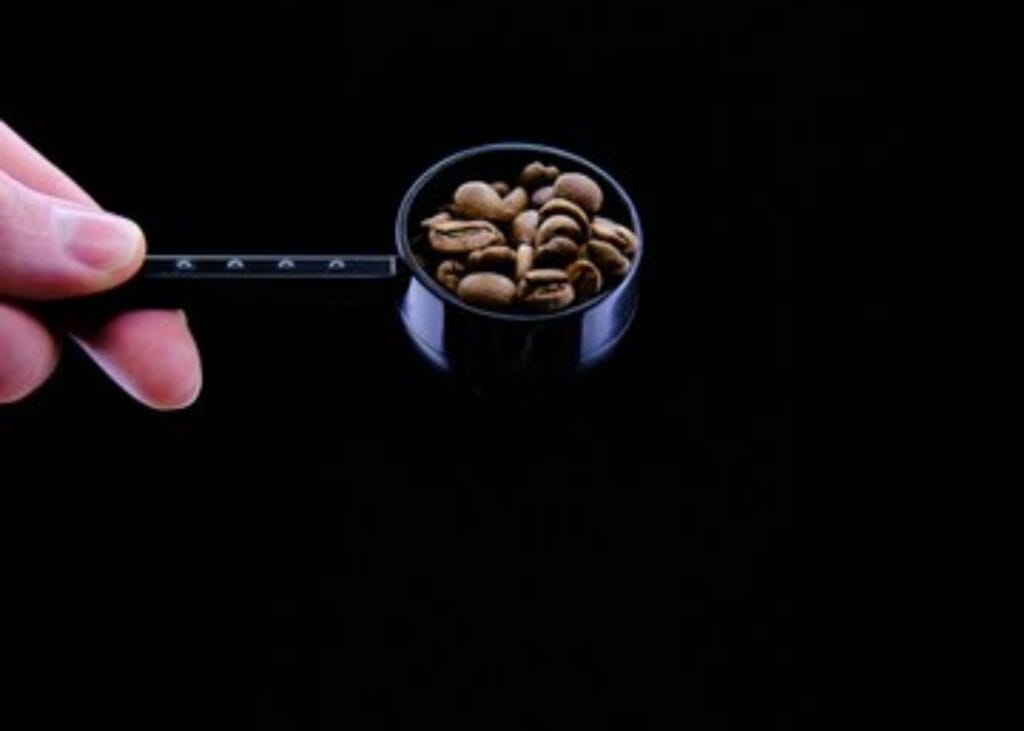 Wondering how much caffeine in one coffee bean? A scoop of coffee beans highlights the answer against black background.