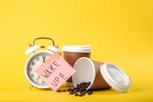 alarm clock, cup with coffee beans with wakeup paper indicating how much caffeine in one coffee bean