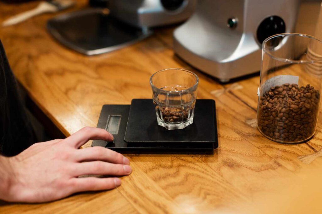 person measuring coffee beans in a glass on a scale