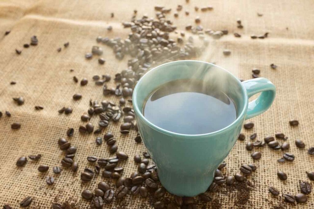 freshly brwed black coffee in a cup with rostaed whole beans around