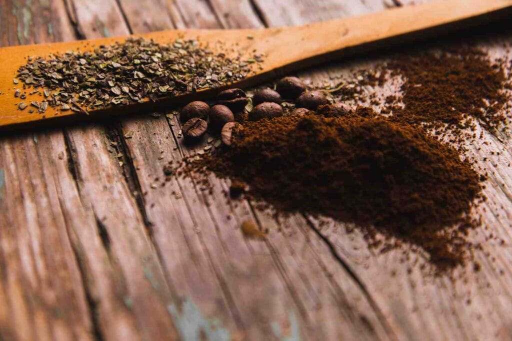 Ground coffee and coffee beans on a wooden surface with a wooden spoon.