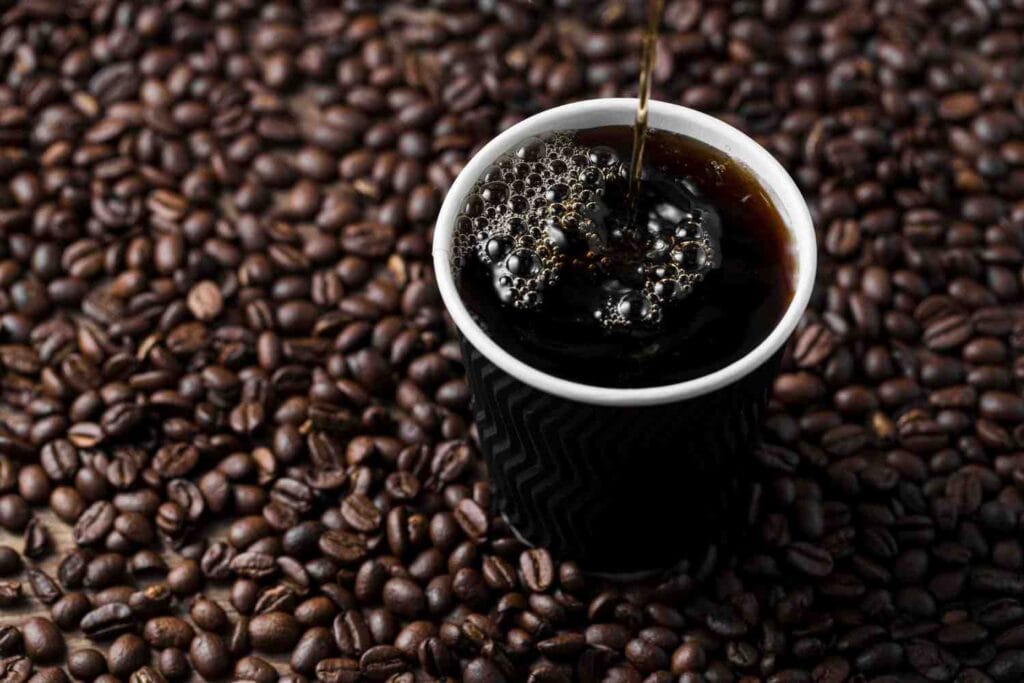 cup of freshly brewed black coffee placed on a bed of roasted coffee beans