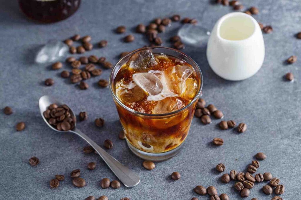cold brew coffee in a glass with whole beans and spoon in surrounding