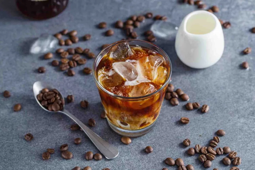 cold brew coffee in a glass with whole beans and spoon in surrounding
